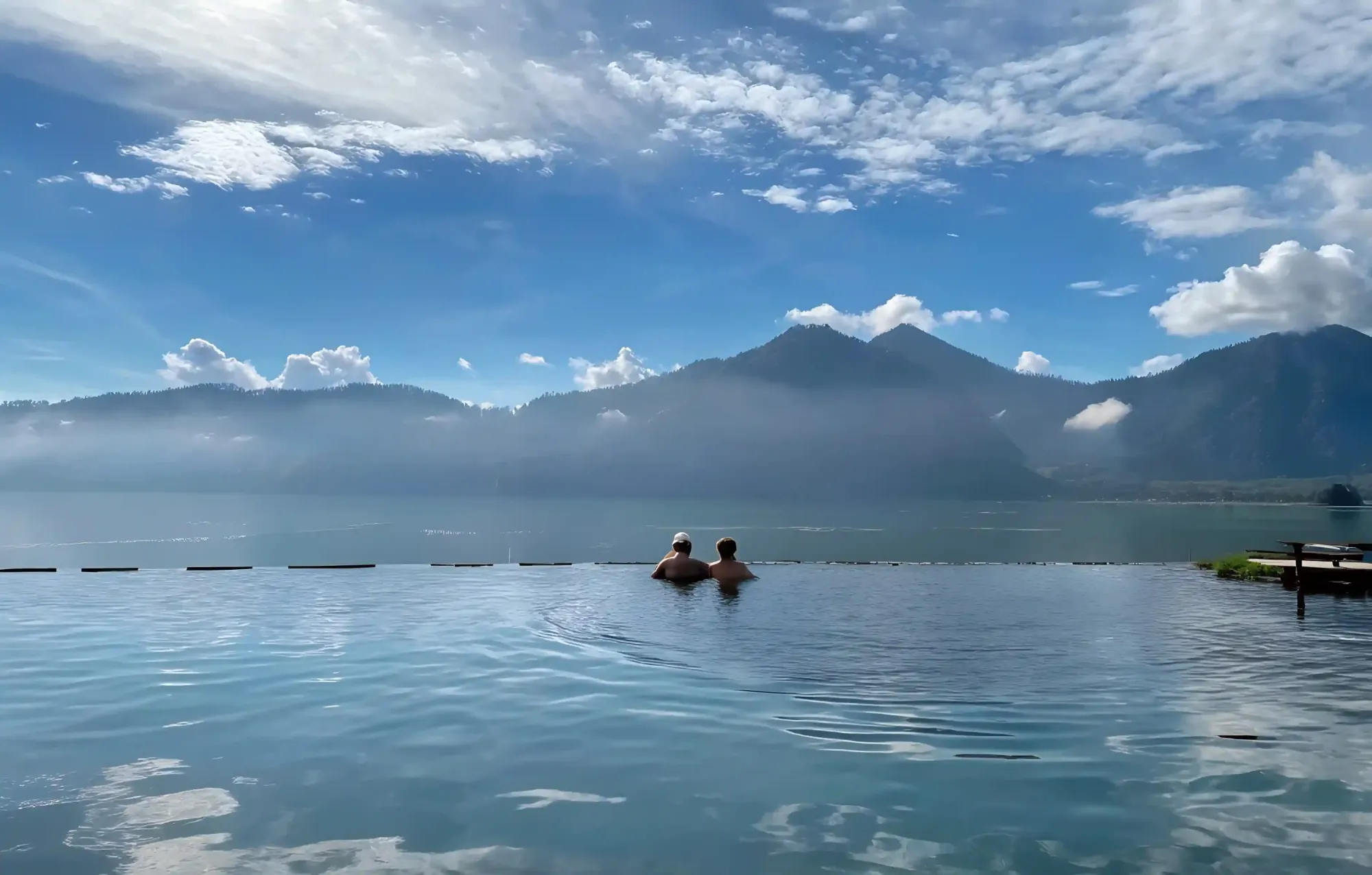 Couple in a hot-spring infinity pool facing Mount Batur and its lake